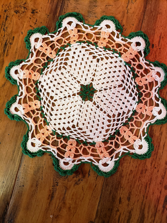 Round crochet doily in off white, peach and green